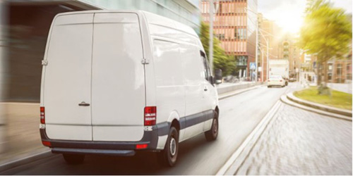 A white van navigates through a city street, surrounded by buildings